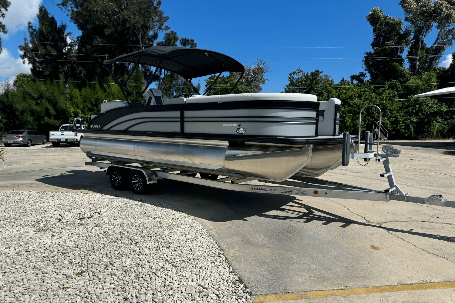 Harris 230 Sunliner 2025 Harris 230 Sunliner pontoon boat on trailer, parked outdoors under clear blue sky.