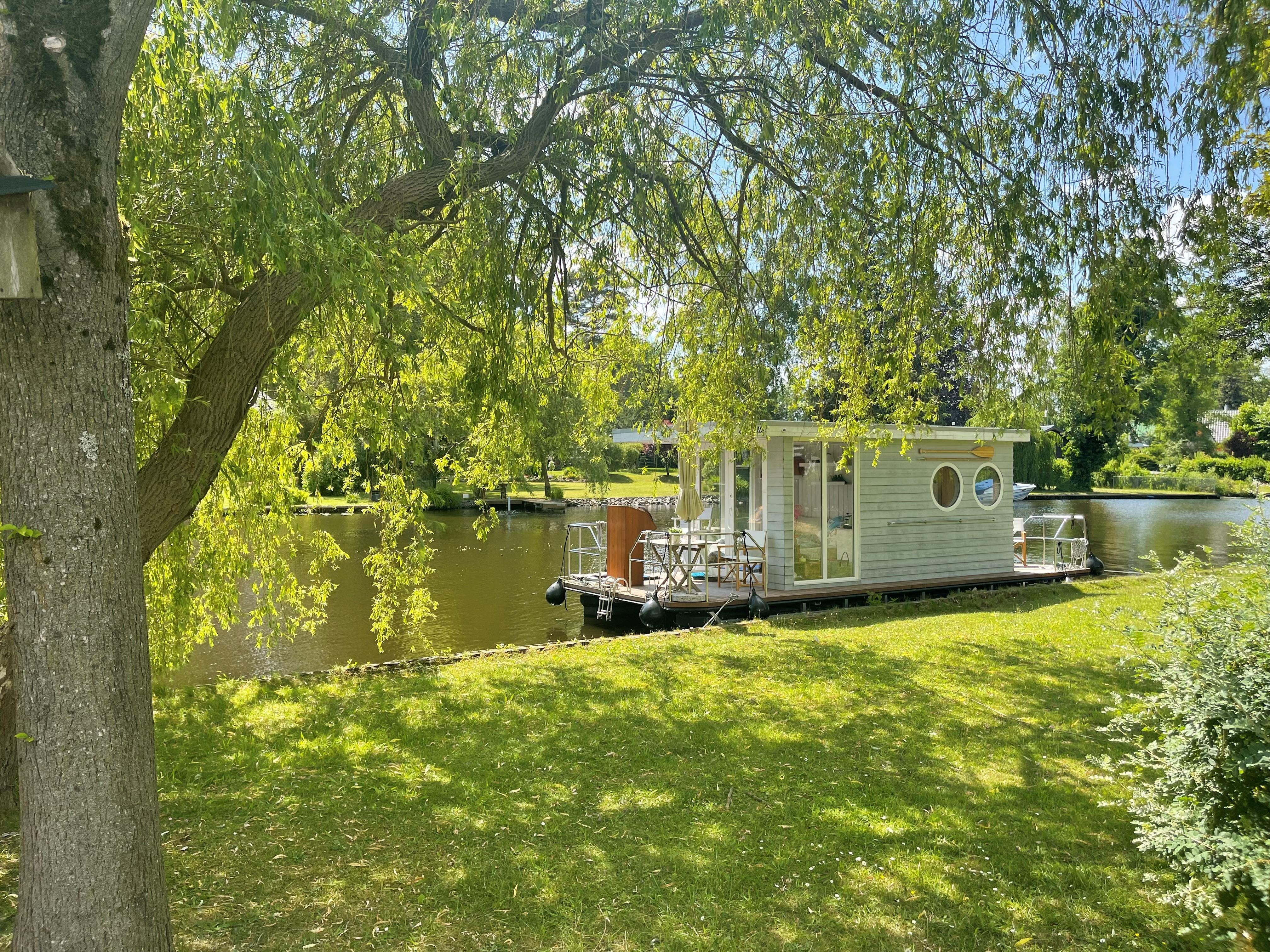 Custom Trimaran Houseboat on a tranquil river, surrounded by lush greenery and trees.