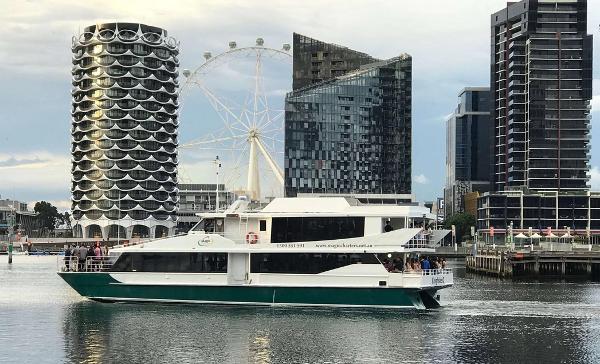 Custom cruising catamaran Custom 1996 cruising catamaran on urban waterway with modern buildings and Ferris wheel in background.