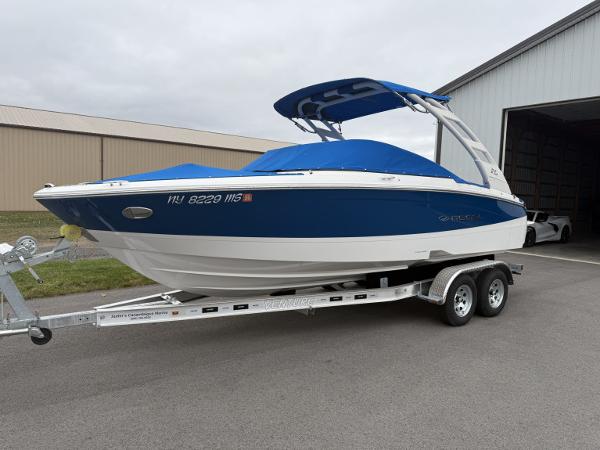 Regal LS2 2023 Regal LS2 boat on trailer, blue and white design, parked outside a warehouse.
