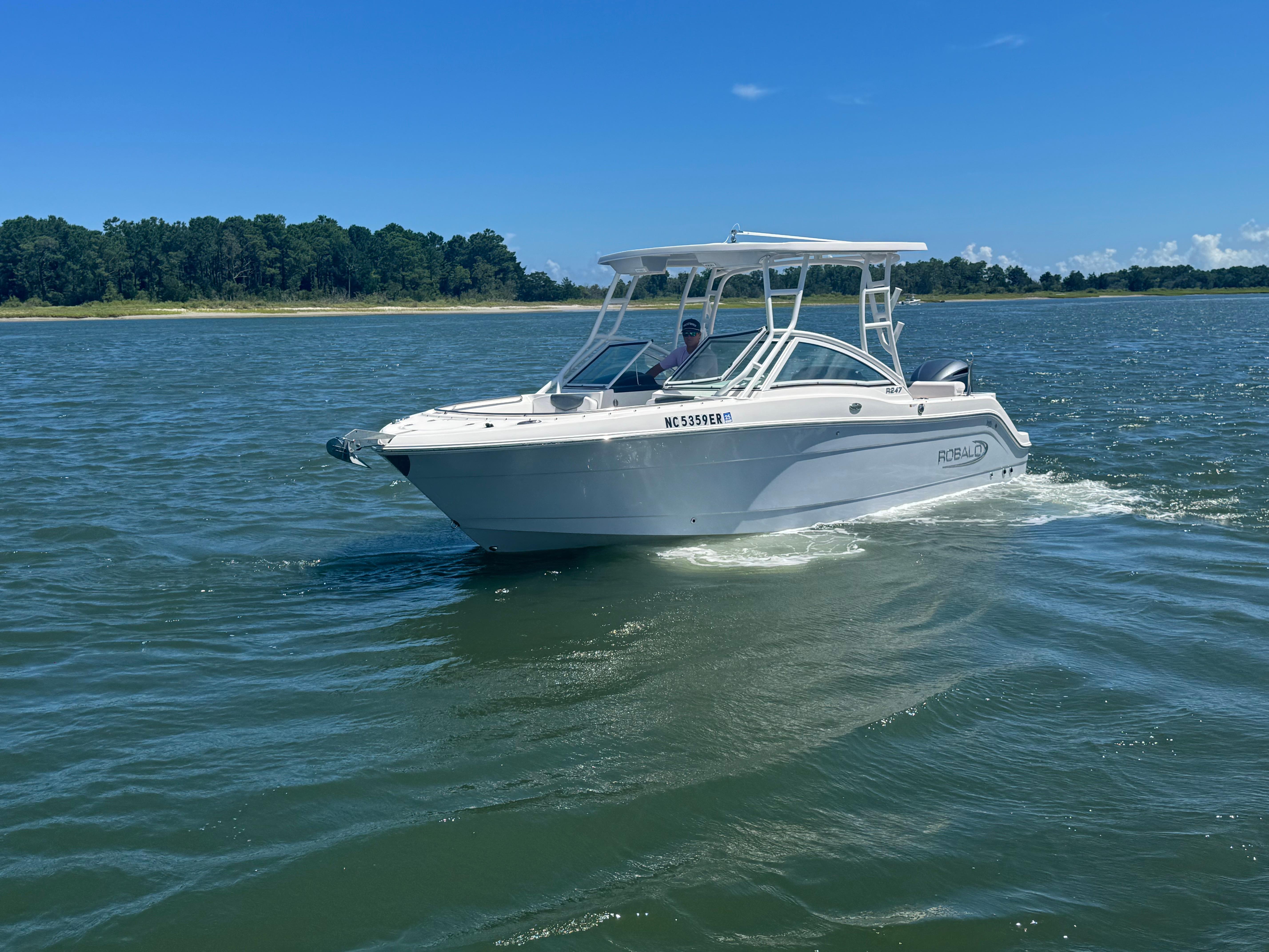 Robalo R247 2021 Robalo R247 boat cruising on a sunny day near a forested shoreline.