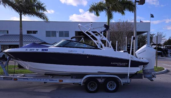 Monterey M225 2023 Monterey M225 boat on trailer, parked near palm trees and building.