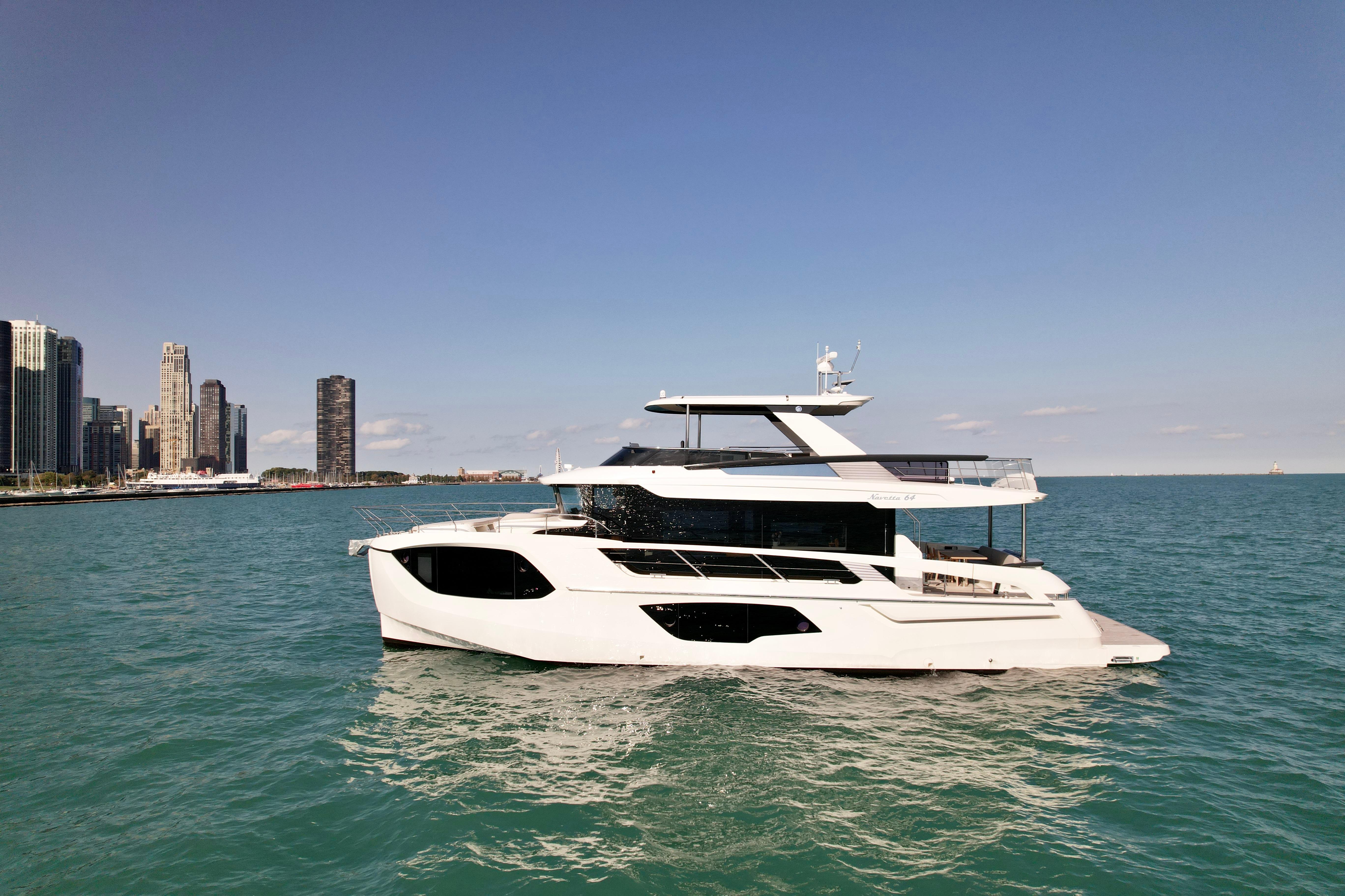 Absolute 64 Navetta 2022 Absolute 64 Navetta yacht cruising near city skyline on a sunny day.