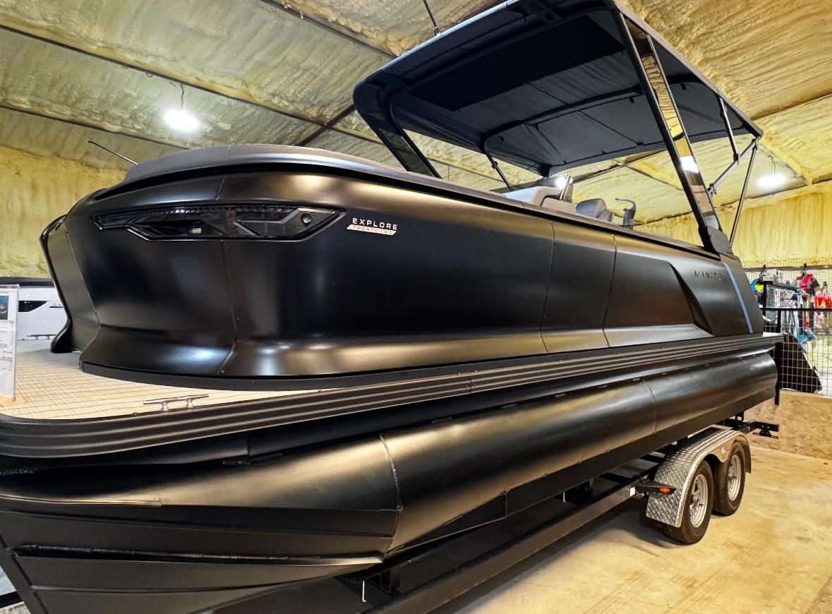 Manitou Explore 2025 Manitou Explore pontoon boat in a showroom, featuring sleek black design.