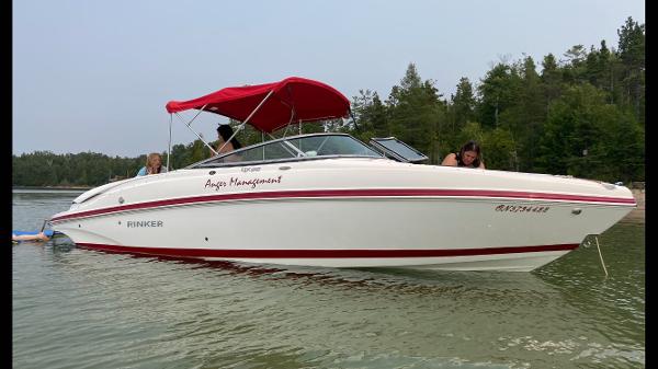 Rinker QX26 BR 2017 Rinker QX26 BR boat with red canopy on calm water, surrounded by trees.
