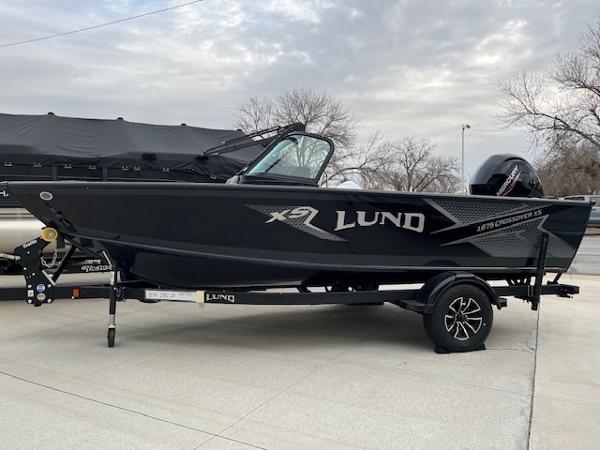 Lund 1875 Crossover XS 2025 Lund 1875 Crossover XS boat on trailer, sleek black design, parked outdoors.