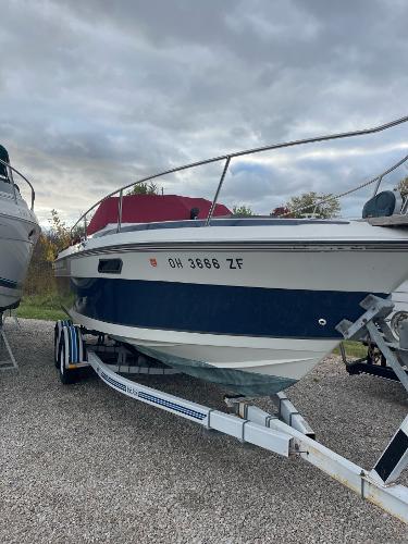 Regal 250 Xl 1988 Regal boat on trailer, blue and white, parked outdoors under cloudy sky.