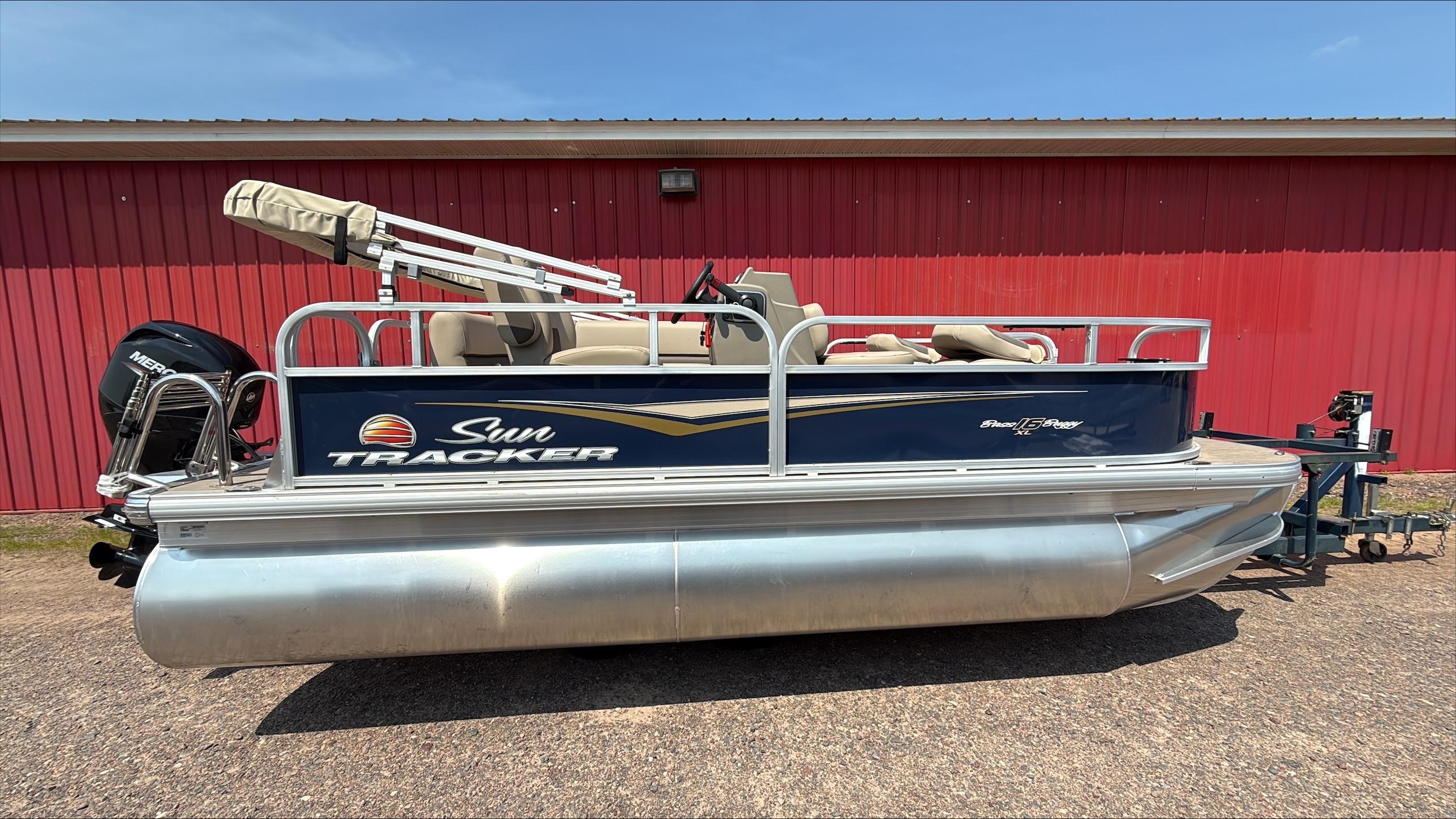 Sun Tracker Bass Buggy 16 XL Select 2025 Sun Tracker Bass Buggy 16 XL Select pontoon boat, parked by a red building.