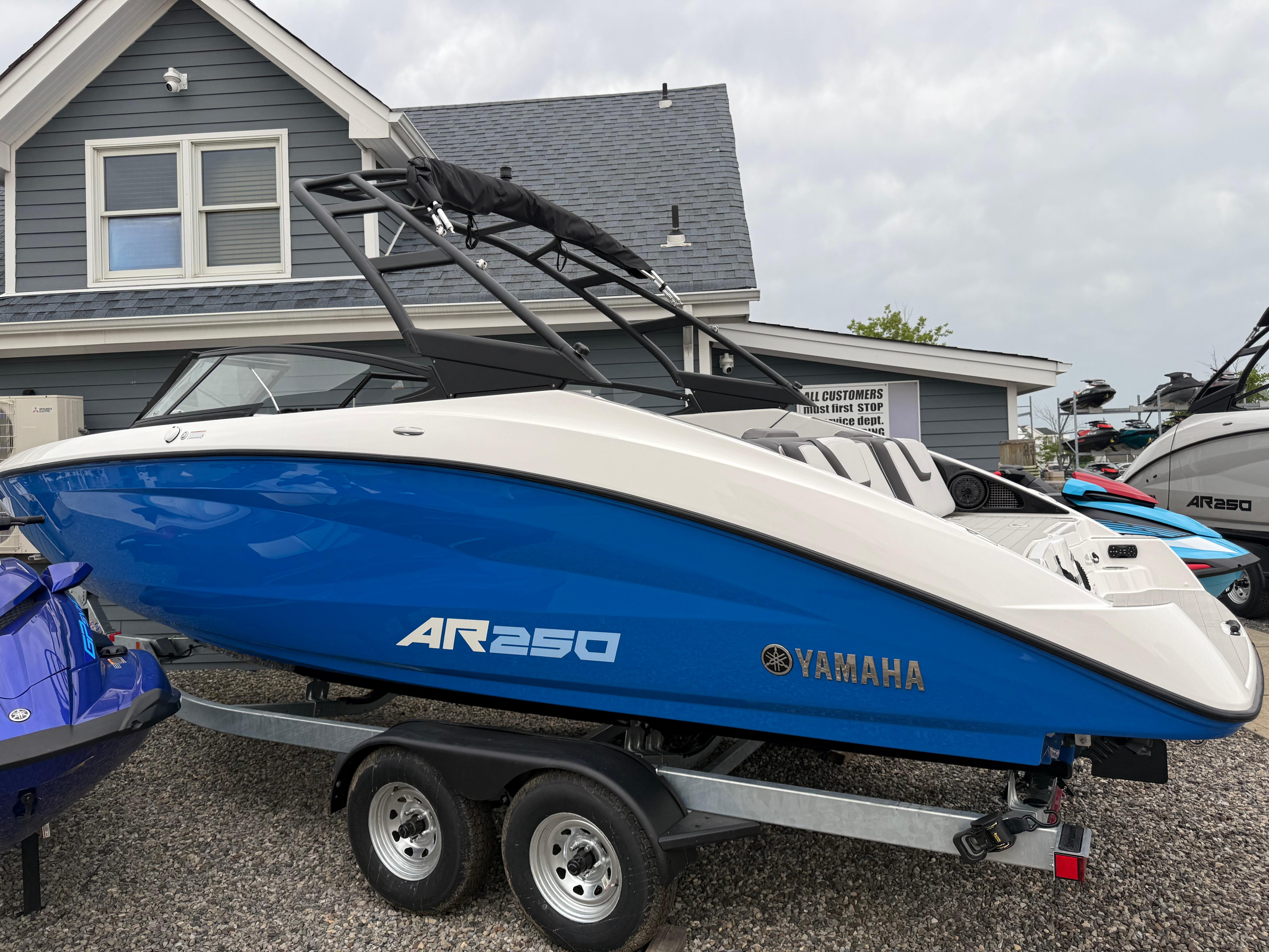 Yamaha Boats AR250 2025 Yamaha AR250 boat in blue and white on a trailer, parked outside a house.