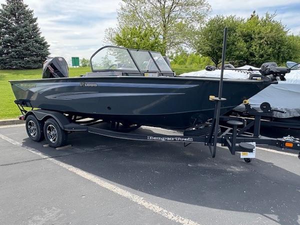 Ranger VX1888 WT 2024 Ranger VX1888 WT boat on trailer in parking lot, surrounded by trees.