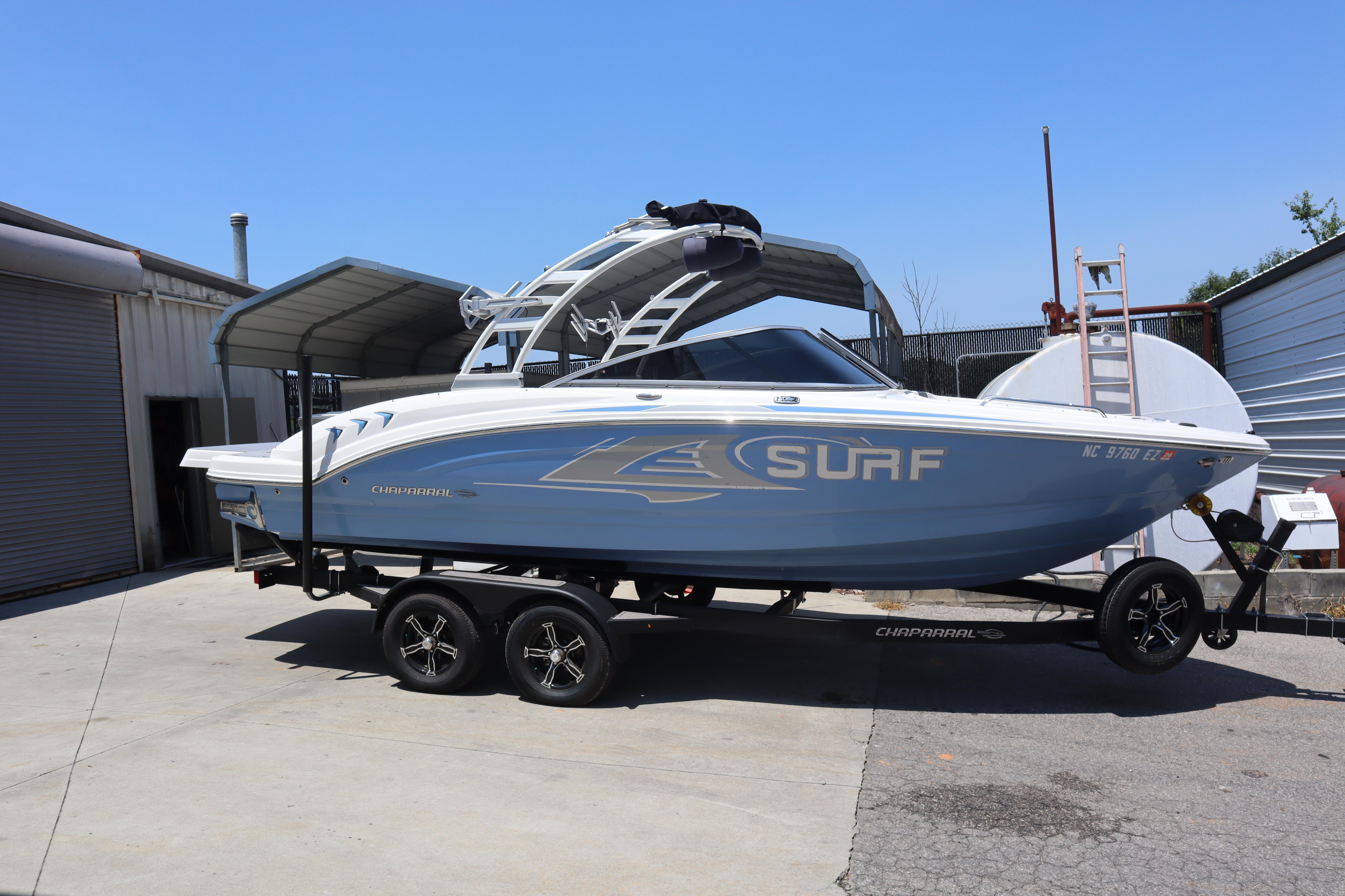 Chaparral 23 Surf 2023 Chaparral 23 Surf boat on trailer, parked outdoors under a metal canopy.