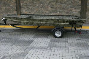 Tracker Grizzly 1860 Utility 2025 Tracker Grizzly 1860 Utility boat on trailer, camo design, parked on brick pavement.