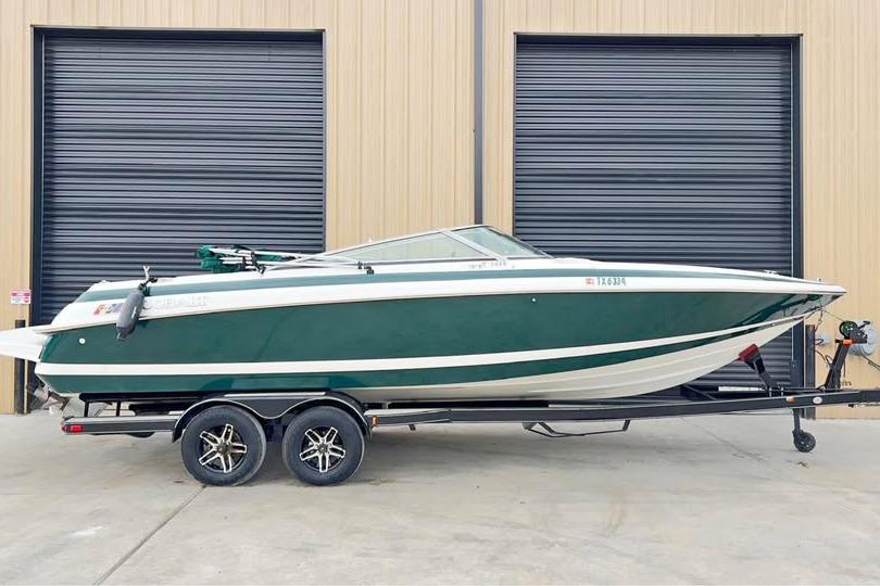 Cobalt 252 2000 Cobalt 252 boat on trailer, green and white, parked outside industrial building.