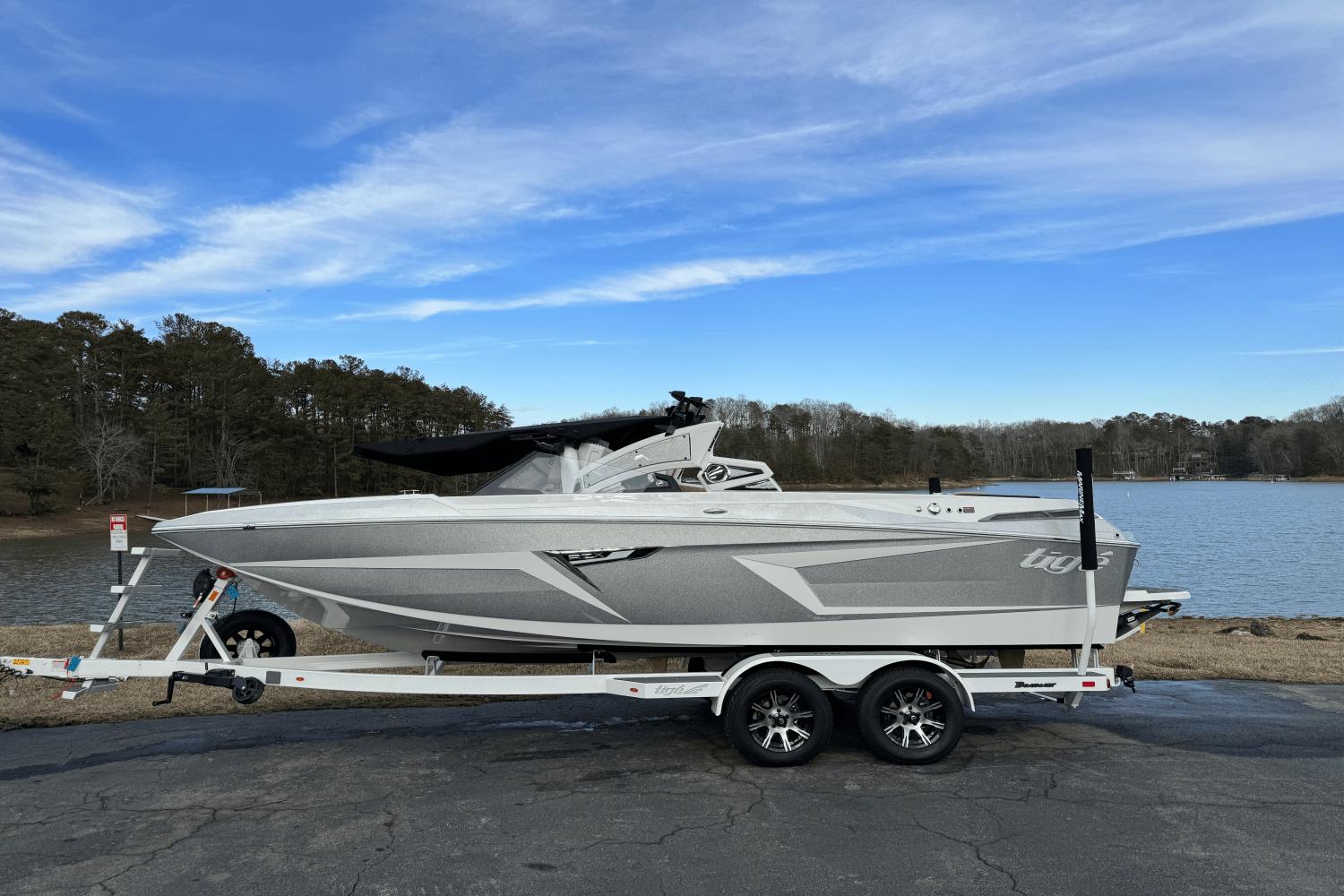 Tigé RZX22 2024 Tigé RZX22 boat on trailer by a lake with a clear blue sky.