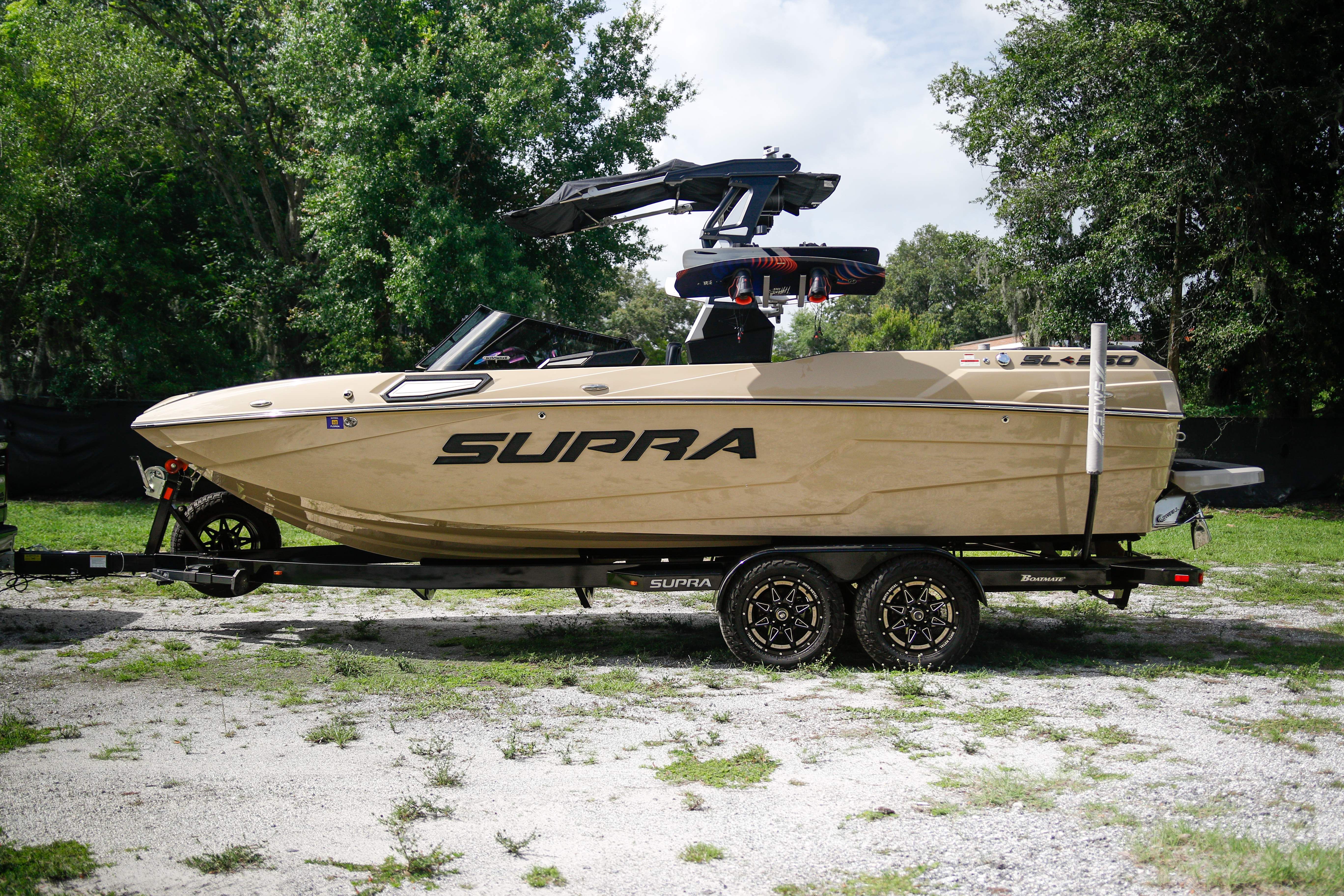 Supra SL 550 2022 Supra SL 550 boat on trailer, parked outdoors with trees in background.