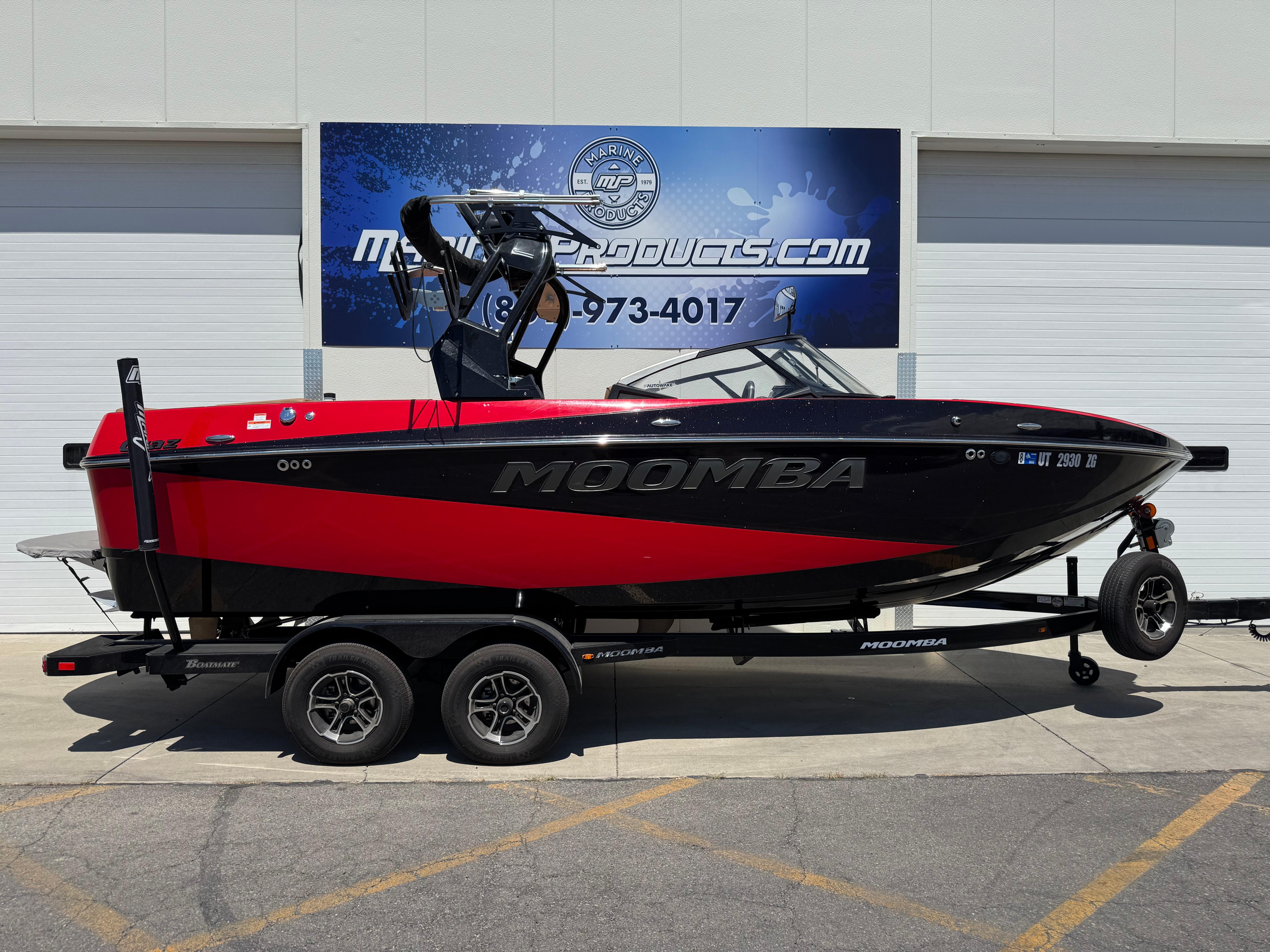Moomba Craz 2024 Moomba Craz boat in red and black on a trailer, parked outside a dealership.