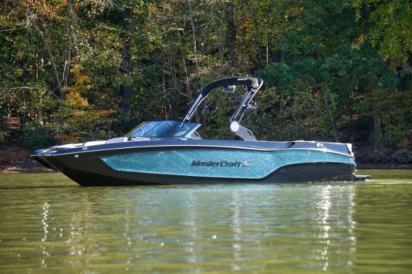 MasterCraft XT24 2025 MasterCraft XT24 boat on a serene lake with lush forest backdrop.