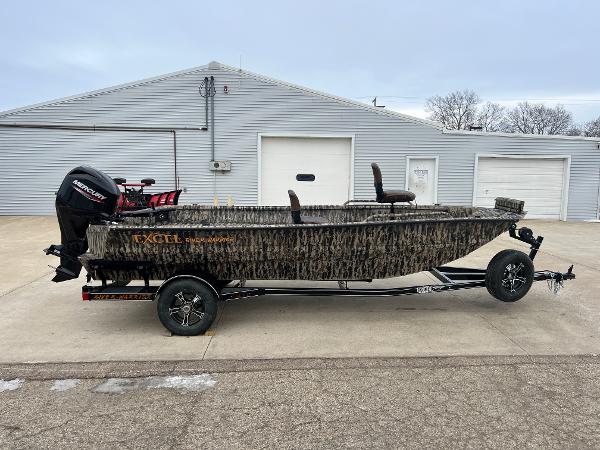 Excel 1751 River Warrior 2025 Excel 1751 River Warrior boat on trailer, camo design, parked outside a garage.