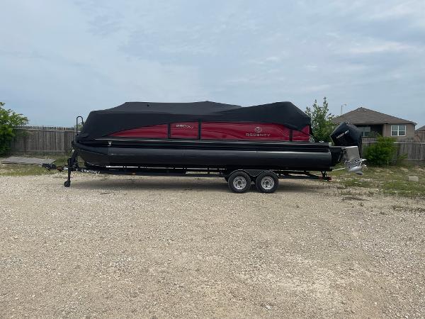 Regency 250DL3 2023 Regency 250DL3 pontoon boat on trailer, covered, parked on gravel lot.