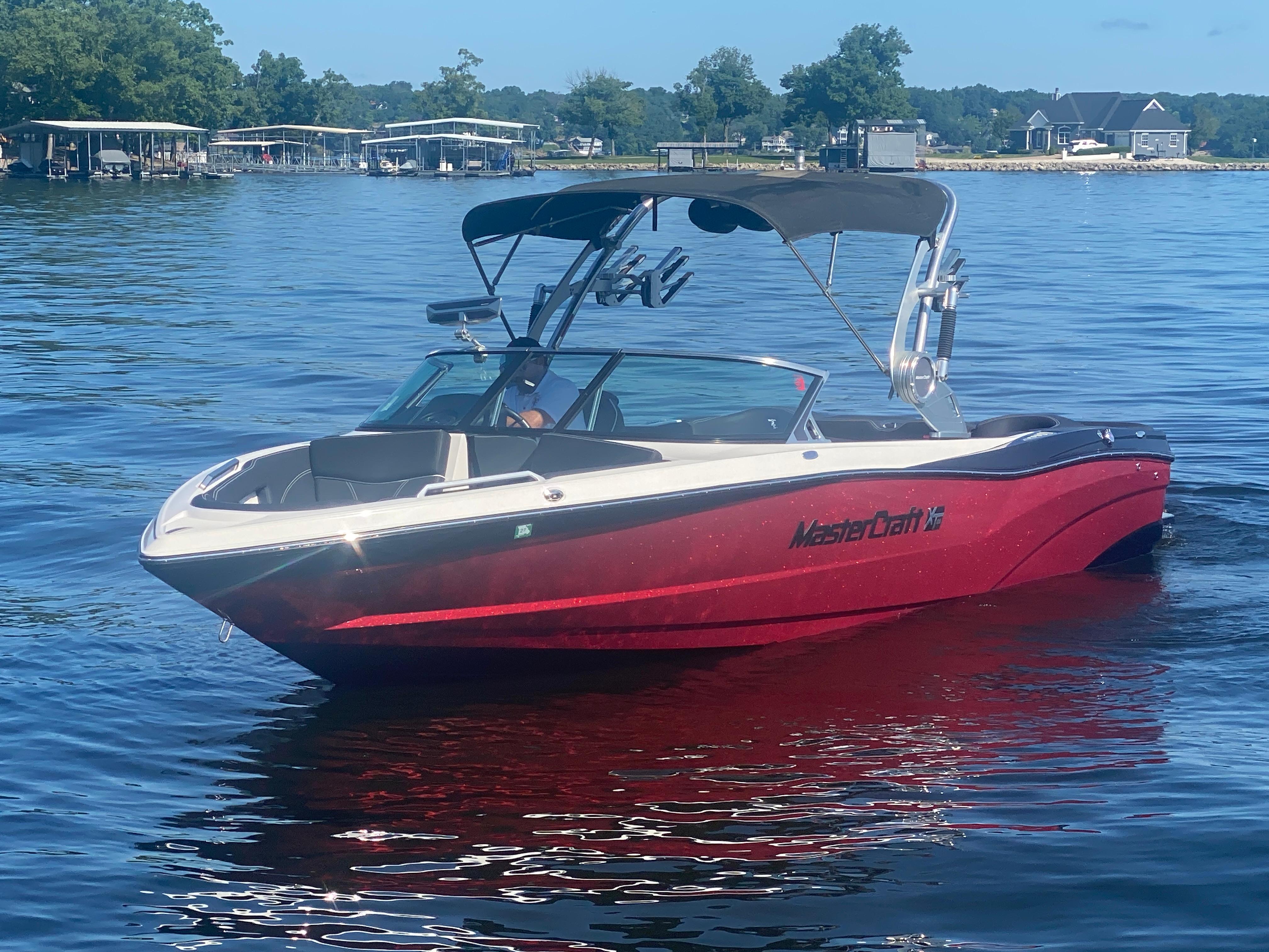 MasterCraft XT25 2020 MasterCraft XT25 boat on a lake, featuring a sleek red design and canopy.