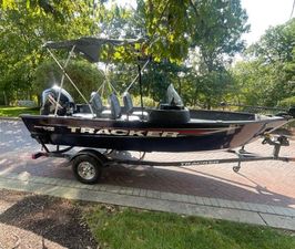 Tracker Pro Guide V-16 SC 2025 Tracker Pro Guide V-16 SC boat on trailer, parked outdoors under trees.