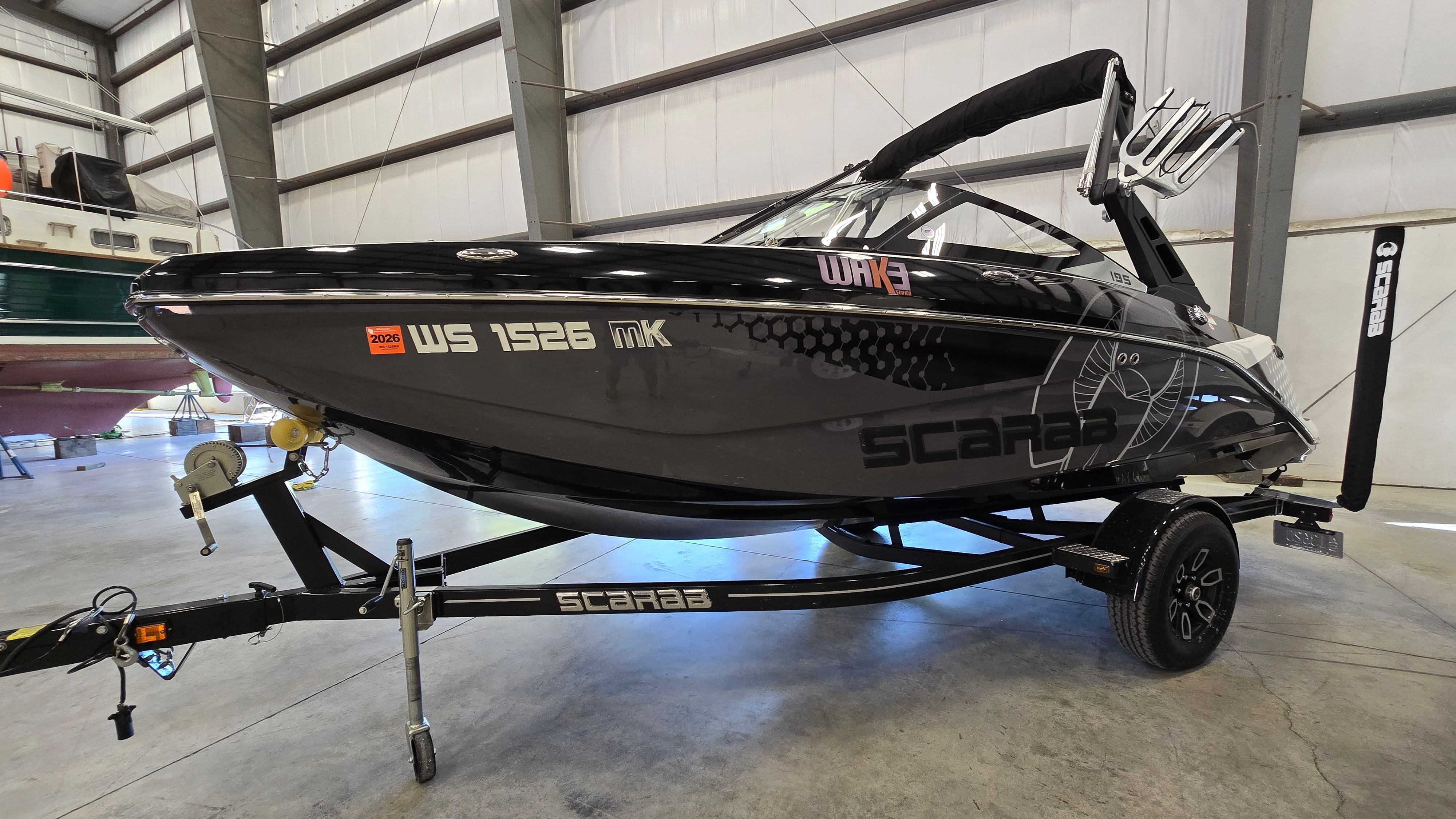 Scarab 195ID IMPULSE 2023 Scarab 195ID IMPULSE boat in a warehouse, black exterior, on a trailer.