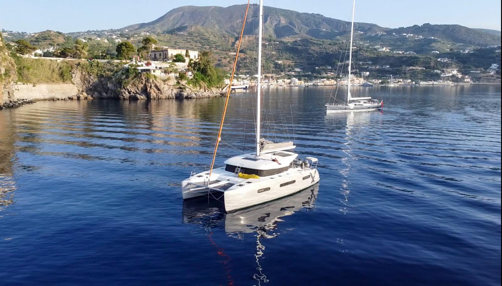 Excess 15 2023 Excess 15 catamaran sailing near scenic coastline with mountains in the background.