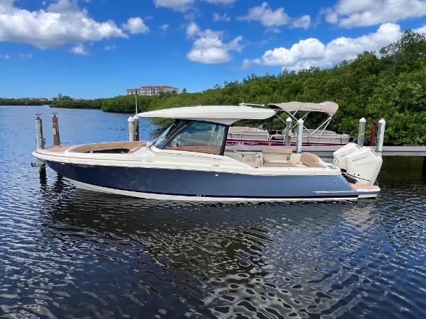 Chris-Craft Calypso 32 2024 Chris-Craft Calypso 32 boat docked on a sunny day, surrounded by lush greenery.