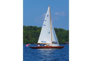 Dragon 29 Vintage 1957 Dragon 29 sailboat on a lake with Canadian flag, clear blue sky.