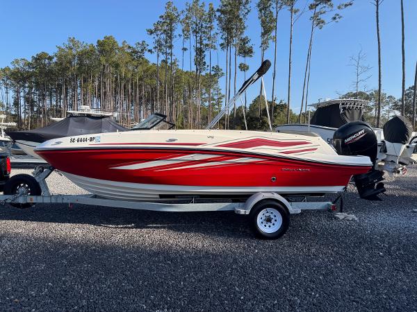 Bayliner VR5 Bowrider OB 2021 Bayliner VR5 Bowrider OB in red, parked on a trailer, surrounded by trees.