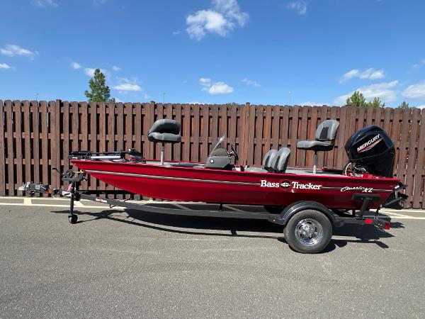Tracker Bass Tracker Classic XL 2025 Tracker Bass Tracker Classic XL boat, red, parked on trailer, wooden fence background.