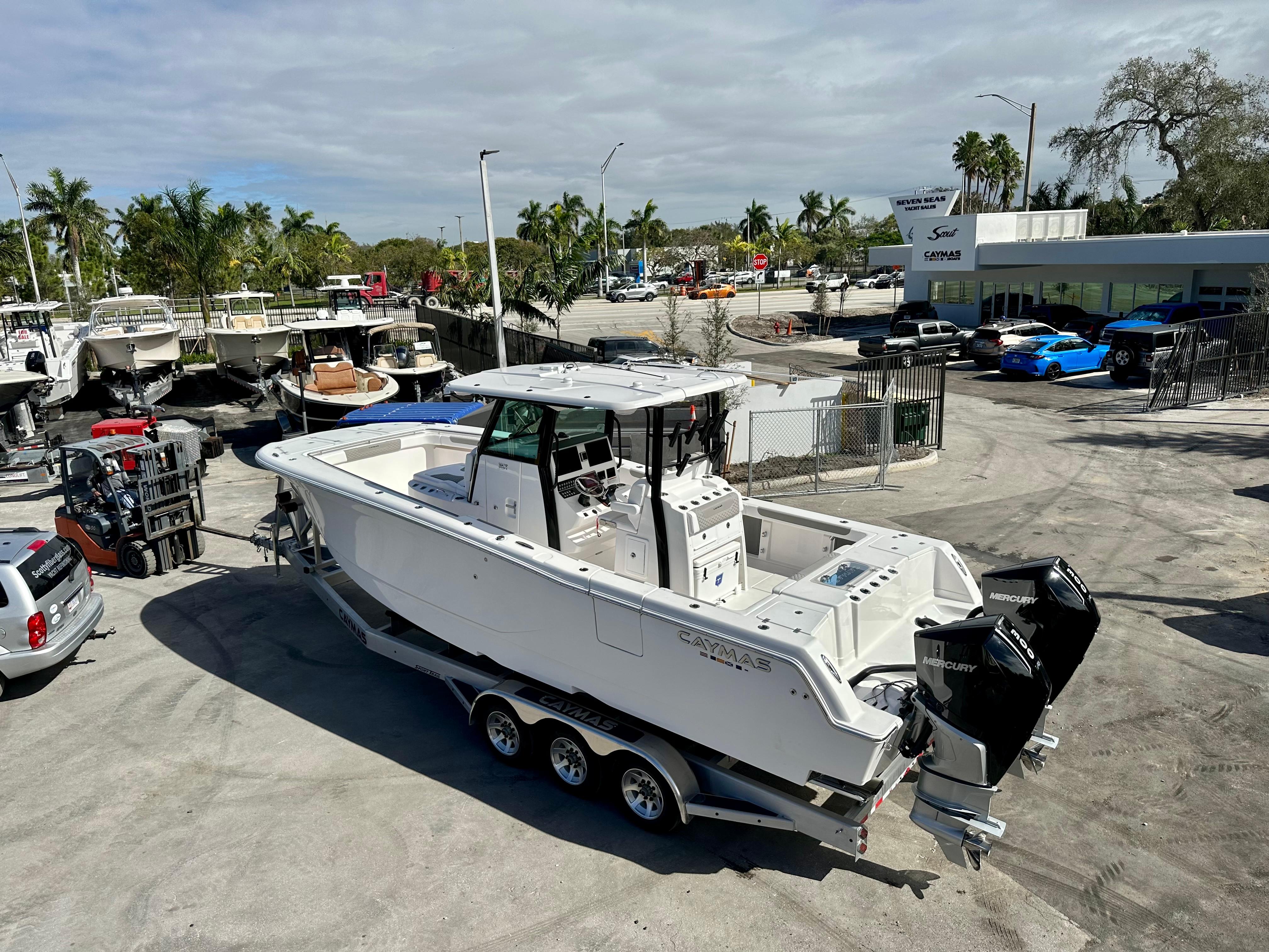 Caymas 30 CT 2024 Caymas 30 CT boat on trailer at dealership, surrounded by palm trees and parked vehicles.