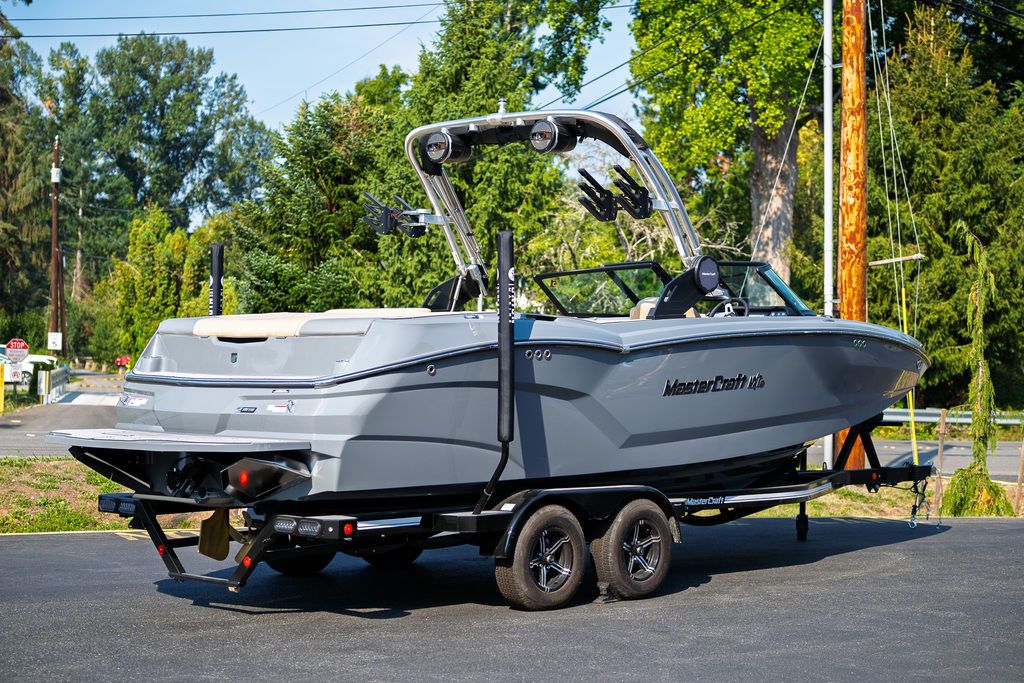 MasterCraft NXT24 2024 MasterCraft NXT24 boat on trailer, parked outdoors, surrounded by trees.