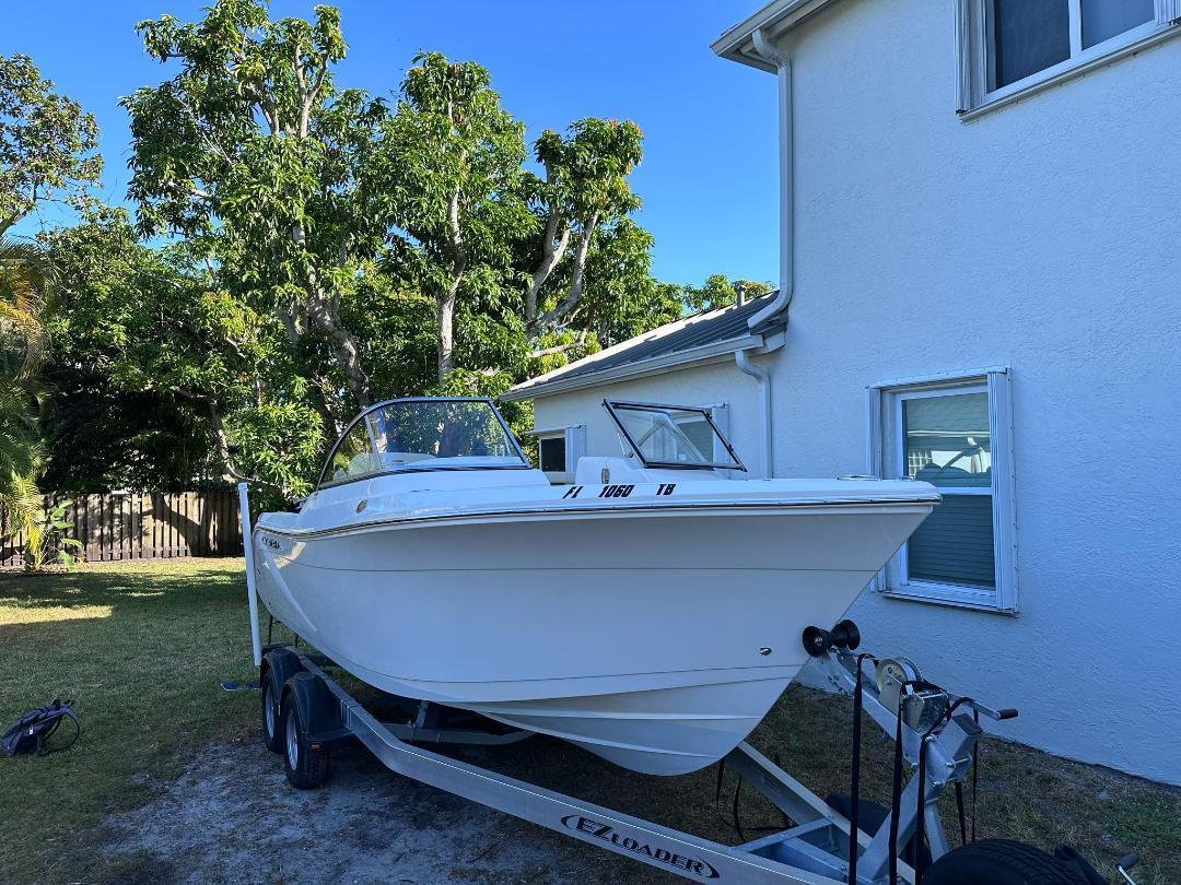 Cobia 220 DC 2022 Cobia 220 DC boat on trailer beside house, surrounded by trees.