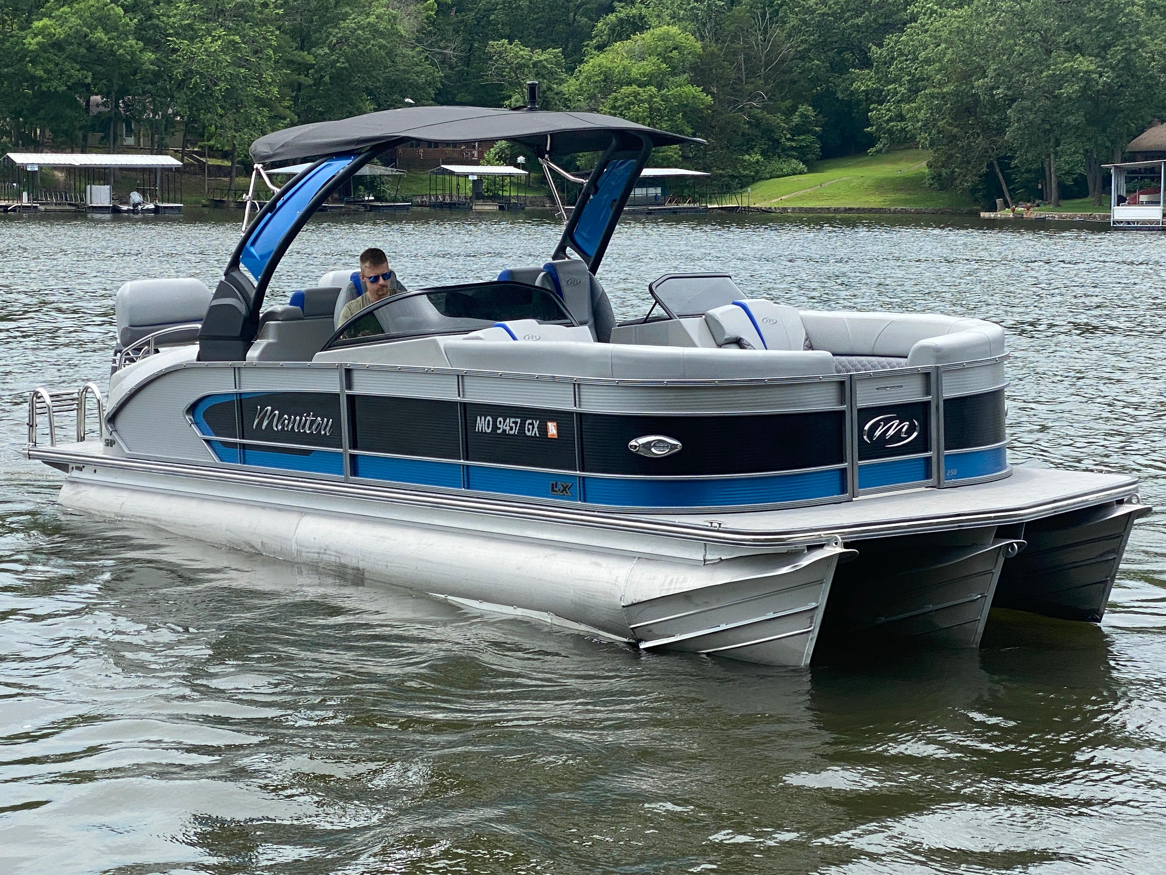 Manitou 25 LX SRW SHP 2022 Manitou 25 LX SRW SHP pontoon boat on a lake with lush greenery.