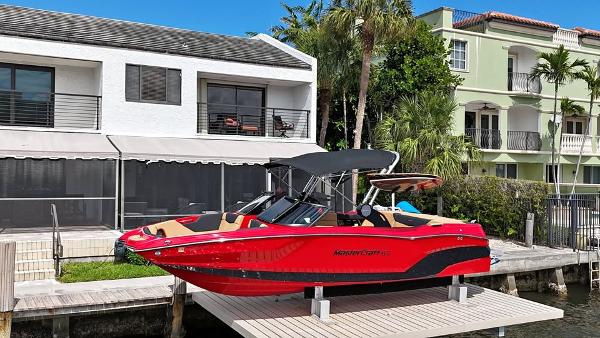 MasterCraft NXT24 2022 MasterCraft NXT24 boat docked near waterfront homes, featuring a sleek red design.