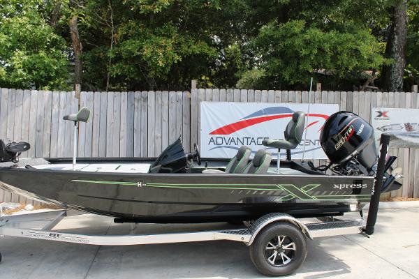 Xpress H18 2026 Xpress H18 boat on trailer, parked outdoors, with trees and fence in background.