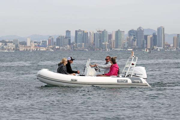 Tide Craft Catalina 13 DEMO Boat Four people on a 2025 Tide Craft Catalina 13 DEMO boat, city skyline in background.