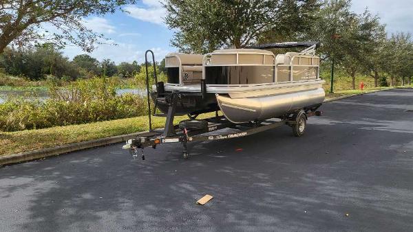 Sun Tracker Party Barge 16 DLX 2025 Sun Tracker Party Barge 16 DLX pontoon boat on trailer, parked near a scenic lake.