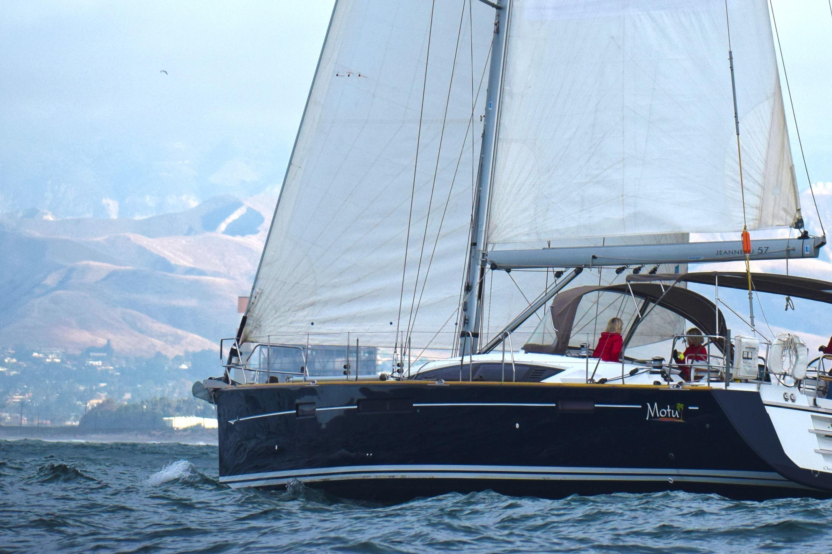 Jeanneau 57 Sailing yacht Jeanneau 57, 2013 model, cruising on open water with mountains in the background.
