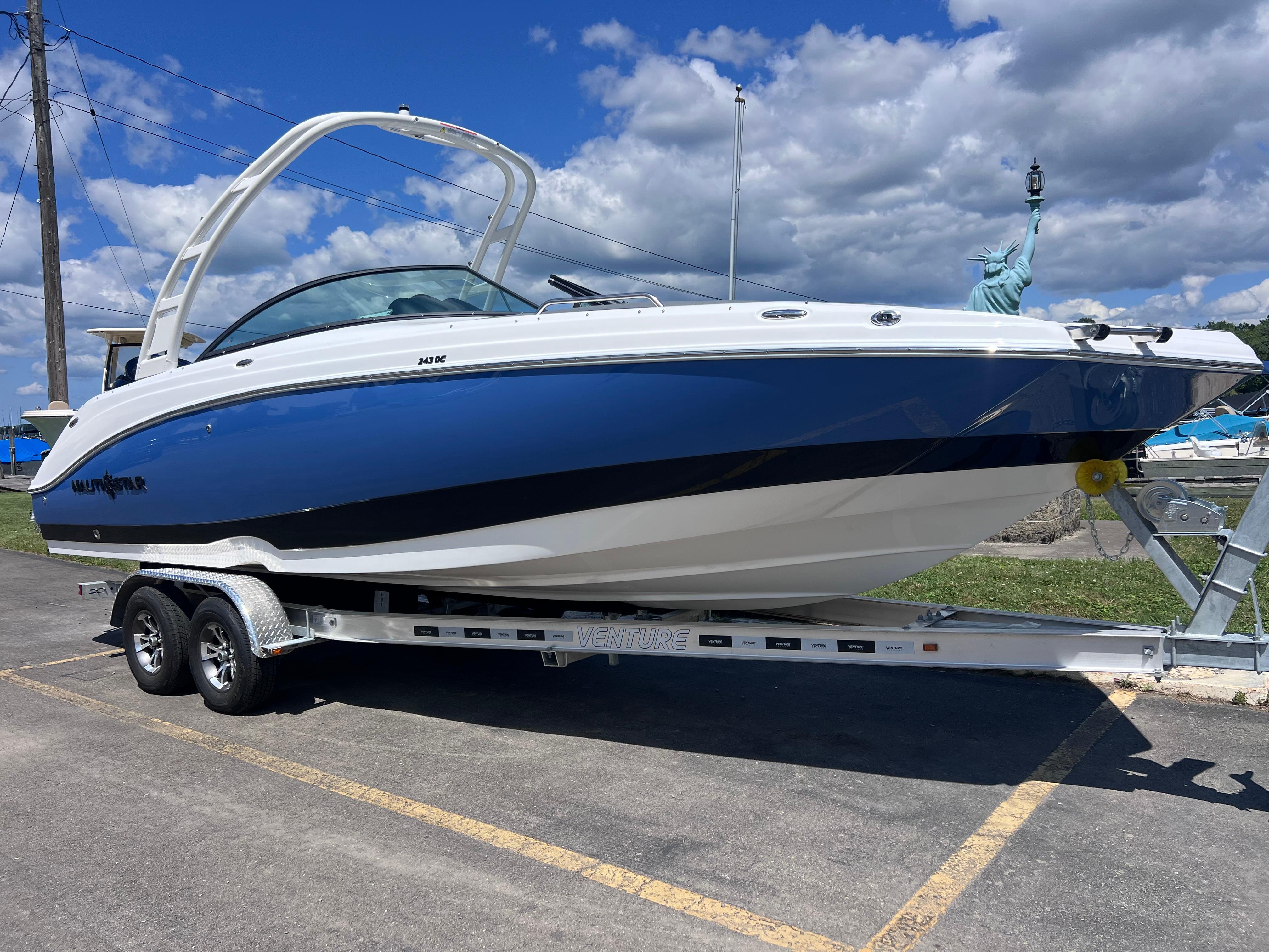 NauticStar 243 DC Deck 2025 NauticStar 243 DC Deck boat on trailer, blue and white, parked outdoors.