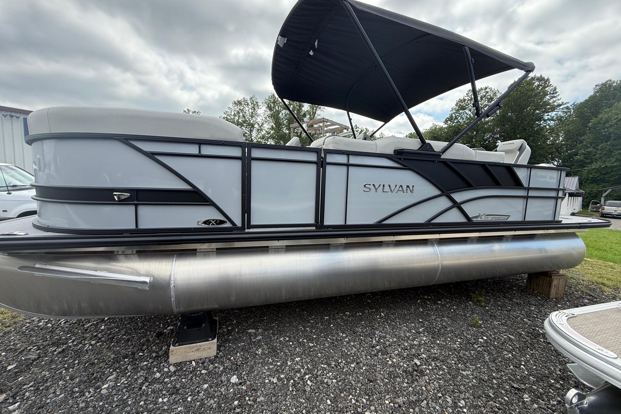 Sylvan X-3 Party Fish 2026 SLYVAN X-3 Party Fish pontoon boat with canopy, parked on gravel.