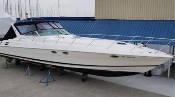 Wellcraft 45 Excalibur 2000 Wellcraft EXCALIBUR boat on stands, white hull, docked near blue-roofed building.