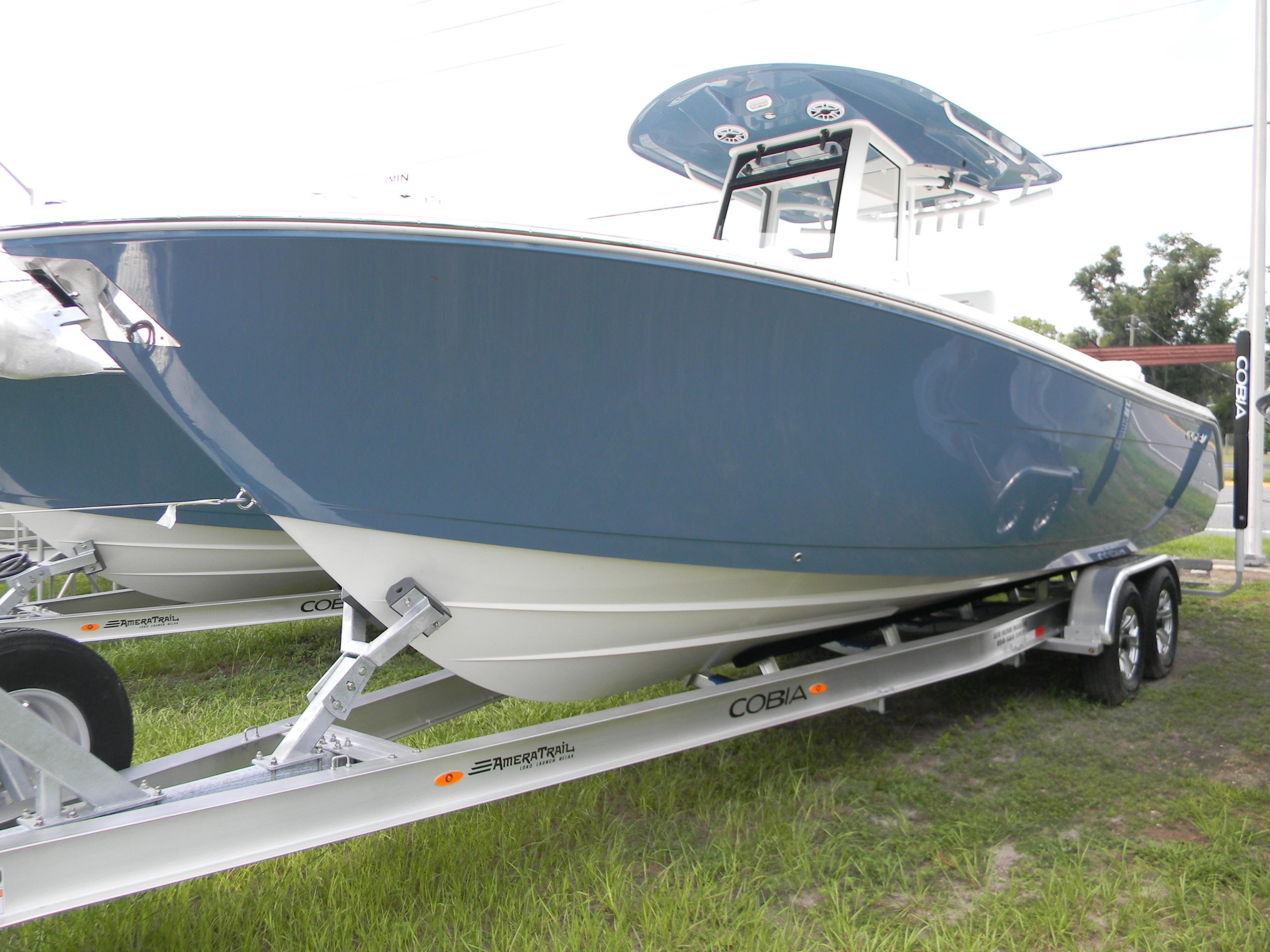 Cobia 285 Center Console 2025 Cobia 285 Center Console boat on trailer, blue hull, parked on grass.