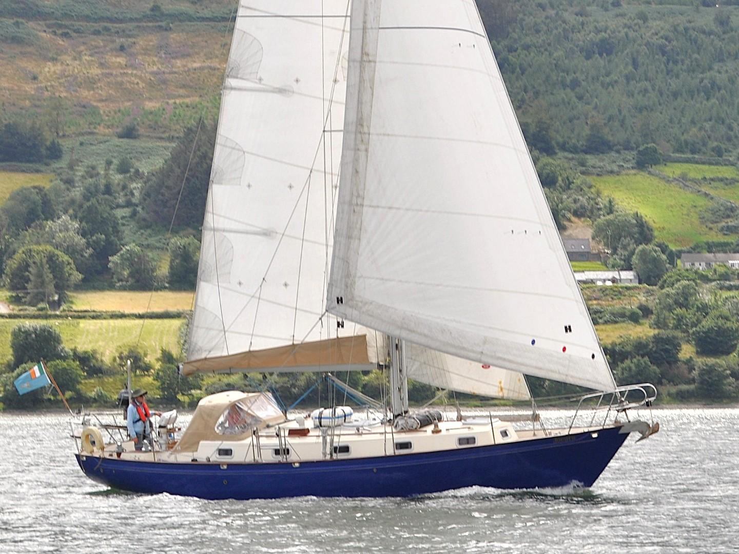 Victoria 38 Sailing yacht Victoria 38, 1998 model, cruising on a scenic lake with lush green hills.