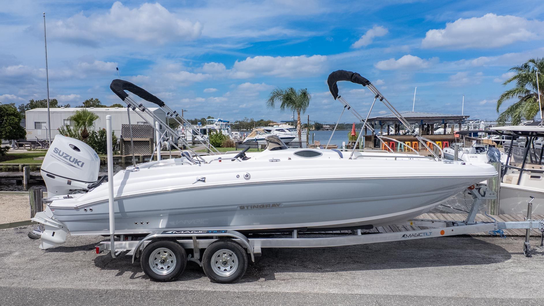 Stingray 212SC 2026 Stingray 212SC boat on trailer, dockside with palm trees and blue sky.