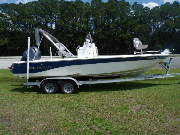 NauticStar 227XTS 2022 NauticStar 227XTS boat on trailer, parked on grass with trees in background.