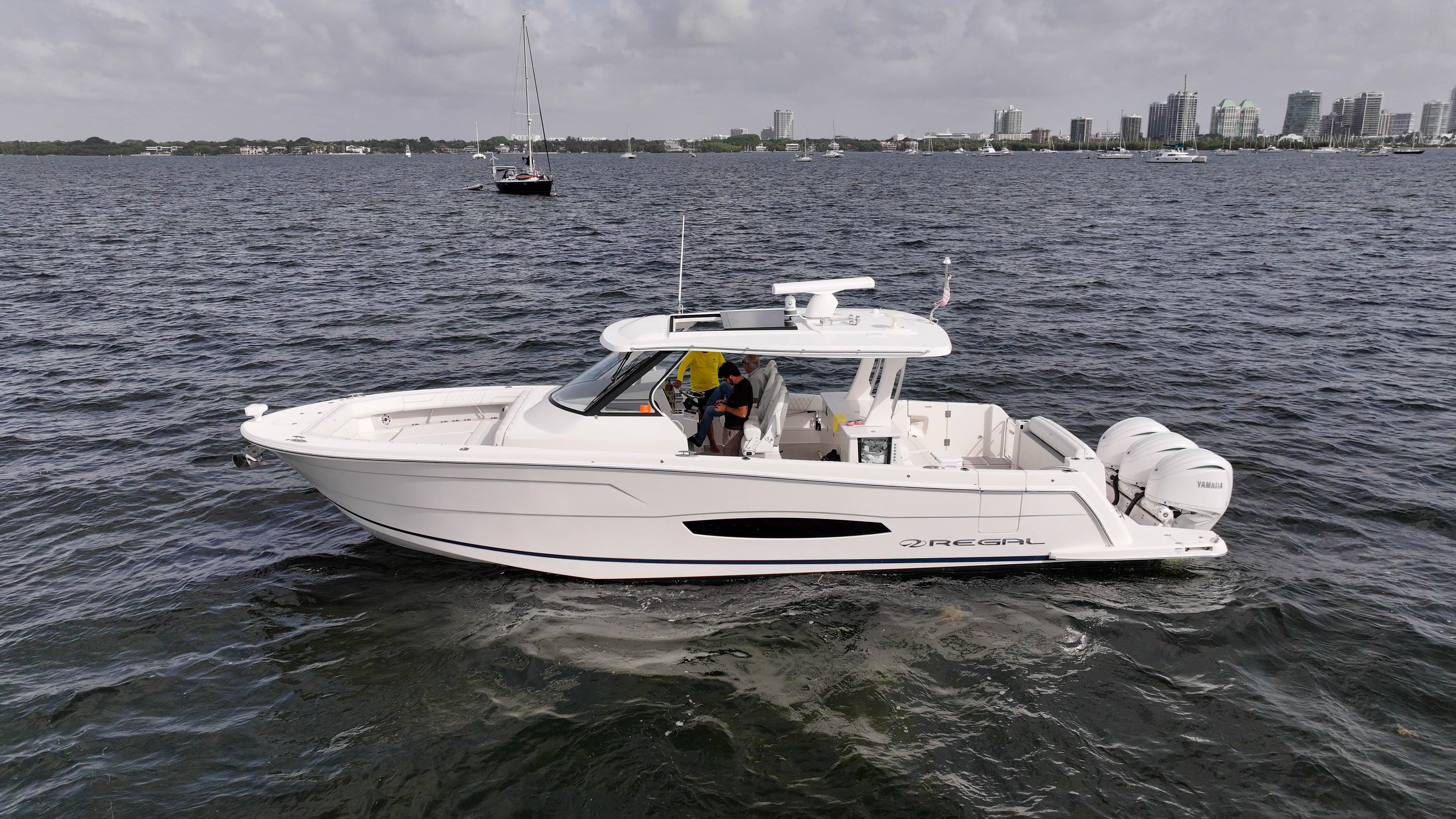 Regal 38 SAV 2023 Regal 38 SAV boat cruising on open water with city skyline in background.