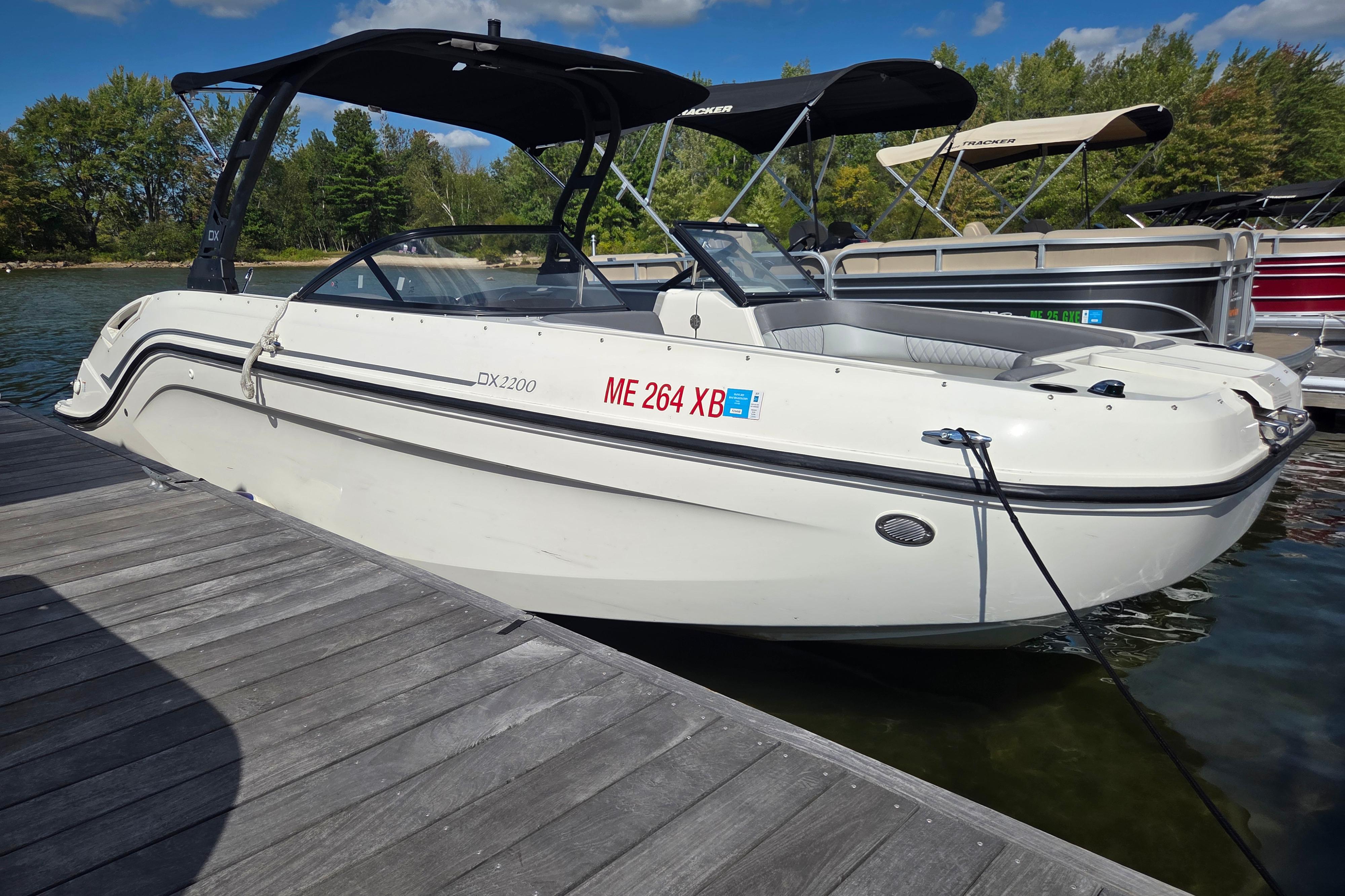 Bayliner DX 2200 2023 Bayliner DX 2200 boat docked on a sunny day with trees in the background.