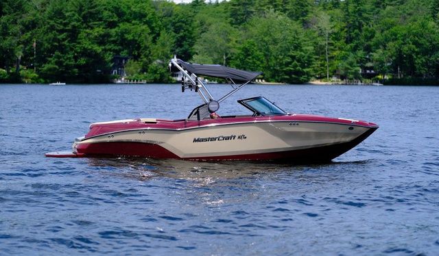 MasterCraft NXT23 2024 MasterCraft NXT23 boat on a lake with lush green trees in the background.
